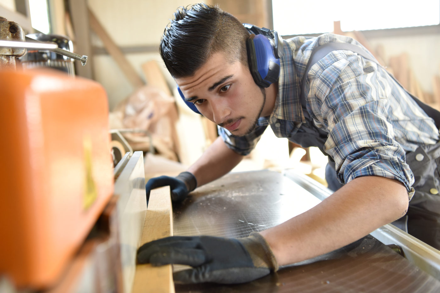 Junger Mann mit Arbeitshandschuhen arbeitet mit Holz an einer Maschine